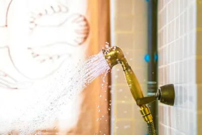 Handheld shower head spraying water against a tiled wall, the fitting a shower filter in Australia screws onto