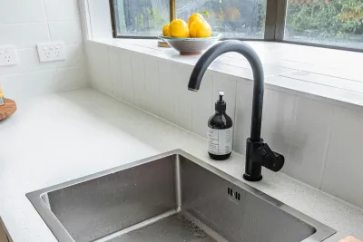 Black mixer tap and stainless steel sink on a stone benchtop in an Australian kitchen, where an under-sink water filter sits in the cupboard below