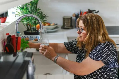 Woman filling a glass from a kitchen mixer tap, the everyday answer to whether you can drink tap water in Australia
