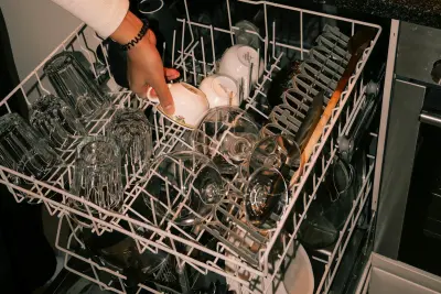 Hand loading cups and wine glasses into the top rack of a dishwasher, the kind of load that shows spots when dishwasher salt is needed but missing
