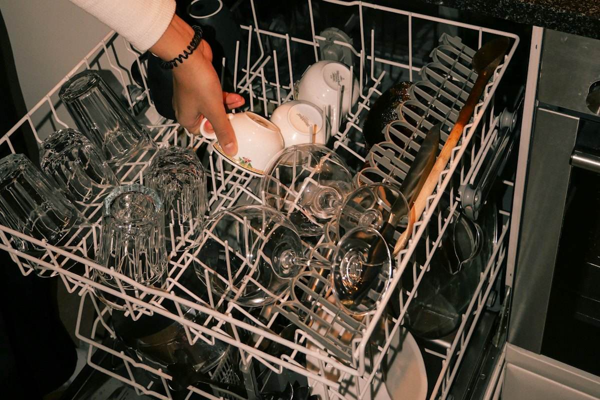 Hand loading cups and wine glasses into the top rack of a dishwasher, the kind of load that shows spots when dishwasher salt is needed but missing