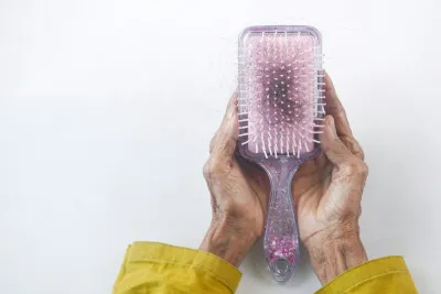 Hands holding a hairbrush with shed strands caught in the bristles, the kind of shedding that makes people ask whether Australian water causes hair loss