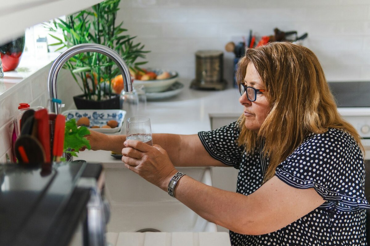 Woman filling a glass at a kitchen tap, the everyday tap water that Australian water filter deals on jugs and cartridges are bought to treat